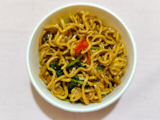 Chewy instant fried noodles in a white bowl, highlighting its texture and deliciousness, against a blurry bowl background.