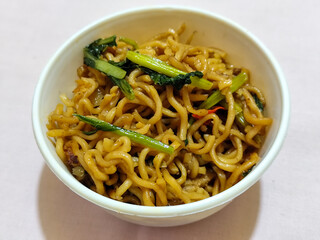 Chewy instant fried noodles in a white bowl, highlighting its texture and deliciousness, against a blurry bowl background.