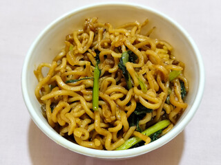 Chewy instant fried noodles in a white bowl, highlighting its texture and deliciousness, against a blurry bowl background.