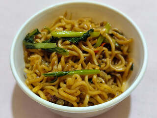 Chewy instant fried noodles in a white bowl, highlighting its texture and deliciousness, against a blurry bowl background.