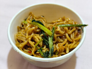 Chewy instant fried noodles in a white bowl, highlighting its texture and deliciousness, against a blurry bowl background.