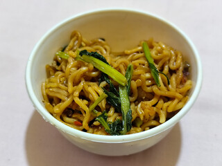 Chewy instant fried noodles in a white bowl, highlighting its texture and deliciousness, against a blurry bowl background.