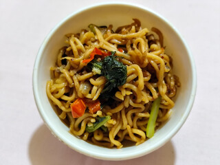 Chewy instant fried noodles in a white bowl, highlighting its texture and deliciousness, against a blurry bowl background.