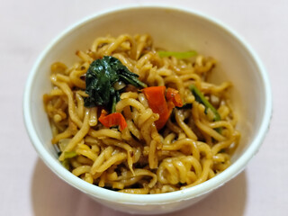 Chewy instant fried noodles in a white bowl, highlighting its texture and deliciousness, against a blurry bowl background.