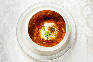 Traditional Russian borscht served in a white bowl, topped with sour cream and herbs, placed on a...
