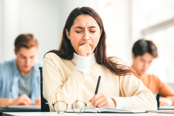 Portrait of tired female student yawning sitting at desk in classroom. Female exhausted from...