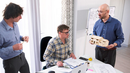 A team of engineers is designing a smart home model. Three men are discussing the design of the building. One of the men holds a model in his hands