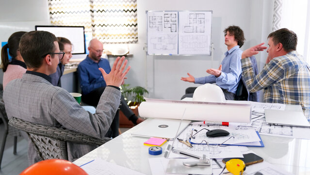 The managers of the construction company discuss the profitability of the project. A group of people gathered around a table and a stand with drawings