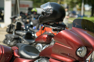 A red touring motorcycle with a black helmet placed on its handlebar is parked among other motorcycles in an outdoor parking area during daylight, representing motorcycle touring culture and road trav