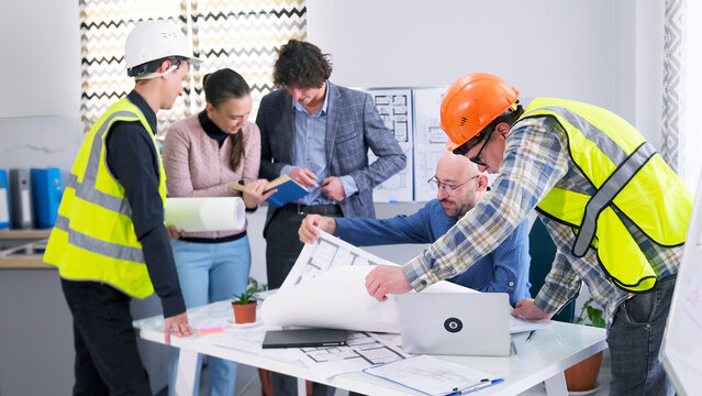 A team of builders, engineers, designers and architects discusses the details of the construction project. A group of people gathered around a table - Powered by Adobe