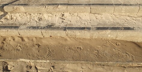 Concrete beach steps, dusted with fine sand, hold the fleeting imprints of a busy day. A mixture of...