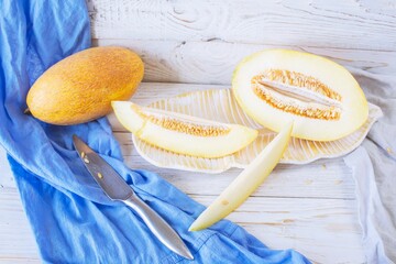 Cut ripe melon. Melon and knife on white wooden background. Top view. Beautiful still life.