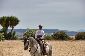 A young, beautiful Spanish woman dressed in riding clothes and wearing a traditional Spanish hat,...