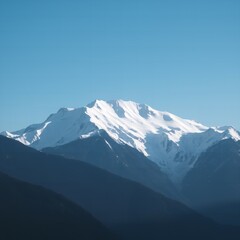 Majestic snow covered mountain peak under a clear blue sky showcasing rugged terrain and deep shadows