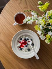 Delicious breakfast - cottage cheese with Greek yogurt, raspberry sauce, blueberries and a cup of tea on a wooden table