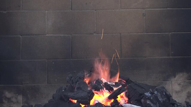 Burning fire with bright flames, glowing charcoal and flying sparks. Close-up of hot embers and wood creating warmth and light, ideal for camping, barbecue, fireplace or relaxation background.