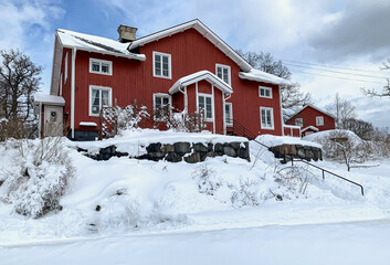 Red wooden two-story house on a snowy March day