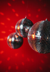 Three shiny disco balls hang against a bright red backdrop, perfect for parties and celebrations.