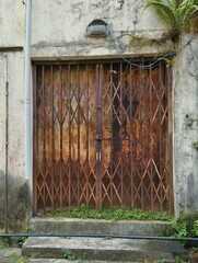 An old, rusty metal grille sliding door,&nbsp;often referred to as a collapsible door grille or a security grille, which serves as a protective barrier for entrances.&nbsp;