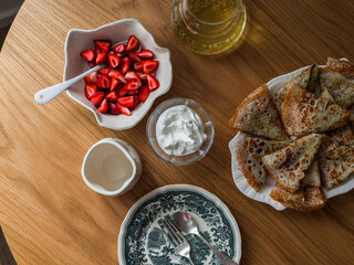 Breakfast served with crepes, fresh cream and strawberries on a wooden table, top view