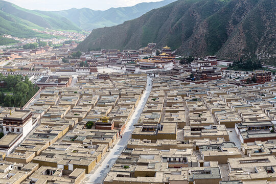 Aerial view of the sprawling Labrang Monastery complex nestled amidst the rugged, mountainous landscape, a sea of rooftops under the vast sky, Xiahe County, China.