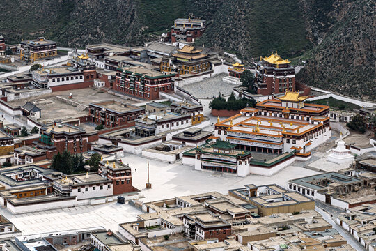 Aerial view of the sprawling Labrang Monastery complex, nestled amongst arid hills, with its golden roofs gleaming under the sunlight, Xiahe, Gansu, China.