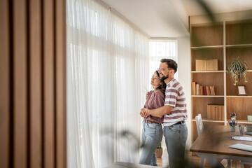 Happy couple embracing and looking out window in new home