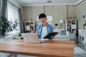 Asian freelancer woman working from home taking notes on documents