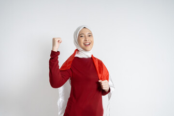 A joyful young Asian Muslim woman wearing a red top and white hijab raises her hands in...