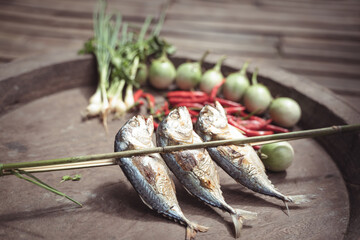 A close-up of fresh ingredients for a rustic Thai meal, featuring grilled fish, chilies, and...