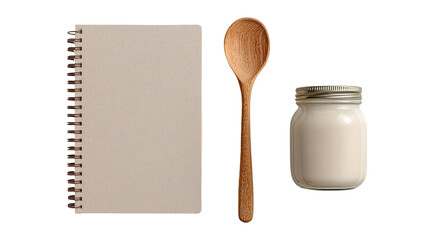 A spiral-bound cookbook, a wooden spoon, and a glass jar of creamy substance