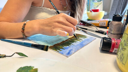 A close-up of a female painter demonstrating her craftsmanship as she works on a canvas with various colors of paint and brushes