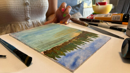 A close-up of a female painter demonstrating her craftsmanship as she works on a canvas with various colors of paint and brushes