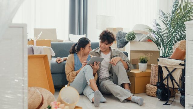 Young happy Asia couple sit on sofa couch use digital tablet online shopping furniture from decoration store in living room at home. Husband wife move new house, Apartment Rent And Ownership Concept.