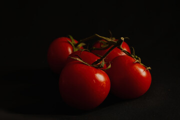 Fresh red tomatoes on the vine with a black background. Close-up of ripe, juicy tomatoes with vibrant color and glossy texture, perfect for food, cooking, and healthy eating concepts.