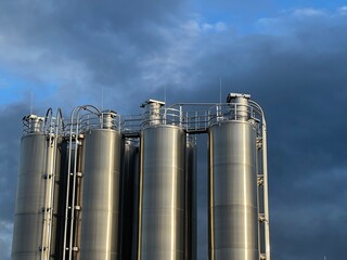 Large stainless steel tanks against a blue sky, representing European industry, storage systems, and modern industrial technology.
