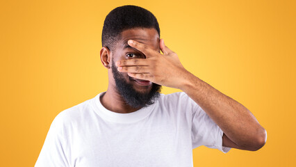 Curious African American Man Peeking Covering Eyes Looking At Camera Through Fingers Posing...