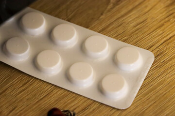 Close-up of white pills in a blister pack placed on a wooden surface, emphasizing health and...