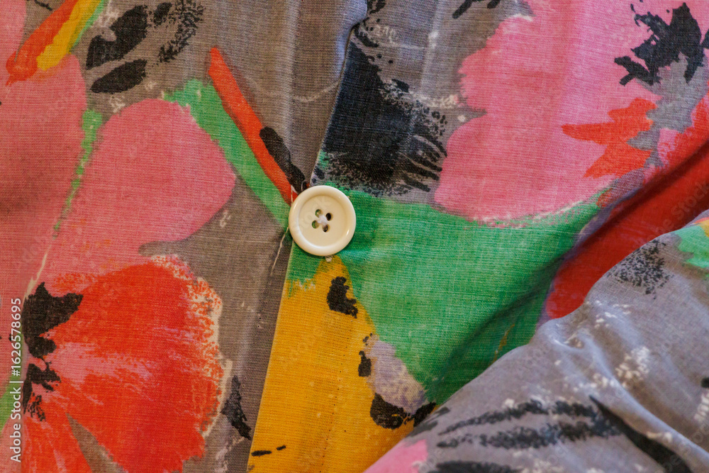 Poster close-up of colorful fabric with floral patterns and a white button, showcasing textile design and f