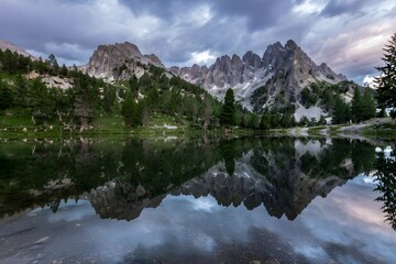 Mountain peaks reflect in the lake water under a cloudy sky at sunset
