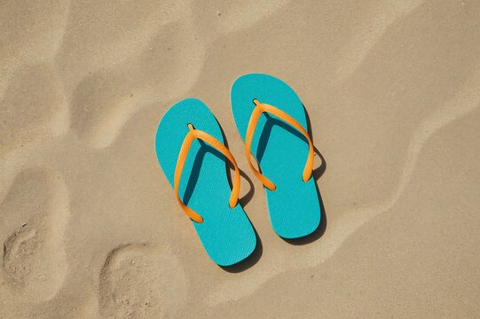 Bright turquoise blue flip flops with yellow straps resting on a sandy beach with subtle footprints