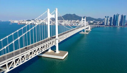 Aerial view of a white suspension bridge over turquoise water, city skyline in the background