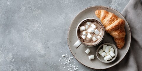 A grey plate holds hot chocolate with marshmallows and a croissant