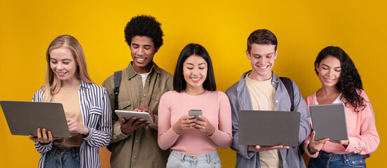Education, knowledge, modern gadgets in college and social networks. Smiling young multiracial students studying, using digital devices, isolated on orange background, copy space, studio shot