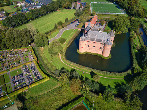 Aerial view of a majestic brick castle surrounded by a moat, reflecting the blue sky and lush greenery, near a cemetery, Helmond, North Brabant, Netherlands.