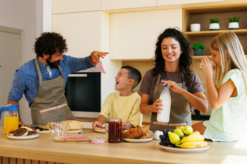 Cheerful family wearing aprons preparing healthy breakfast in modern kitchen and having fun
