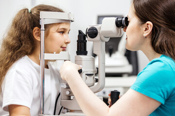 Young girl undergoing eye examination with ophthalmologist using slit lamp in a bright clinical...