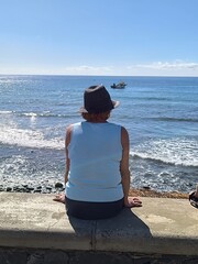 Adult woman, back view, gazing at the sea on a sunny day. Female tourist, back view, breathing in...