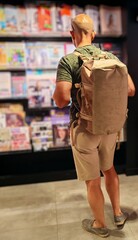 A man seen from behind choosing a magazine for his trip. A young adult man, seen from behind, at an...