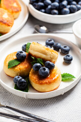 Appetizing cheesecakes with sauce and blueberries on a light background